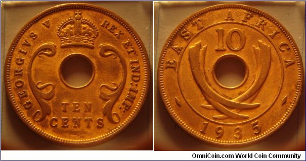 East Africa | 
10 Cents, 1935 | 
31 mm, 11.14 gr. | 
Bronze | 

Obverse: Denomination below centre hole | 
Lettering: GEORGIVS V REX ET IND:IMP: TEN CENTS | 

Reverse: Curved tusks flank the centre hole, numeral denomination above, date below | 
Lettering: EAST AFRICA 10 1935 |
