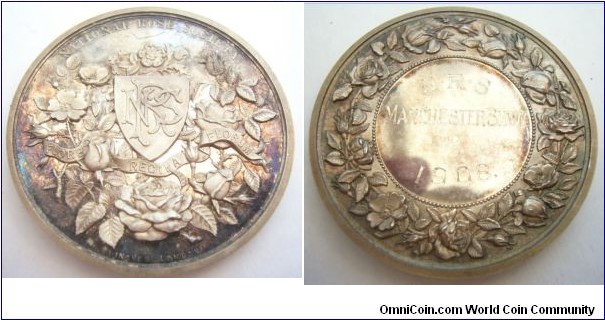 1908 UK National Rose Society Manchester Show Medal. Silver: 42MM./38.3 gms.
Obv: Shiled of NRS surround by roses & banners. Legend NATIONAL ROSE SOCIETY. Rev: Wreath of roses surround outer ram. Center engraved N.R.S.MANCHESTER SHOWN 1908.
