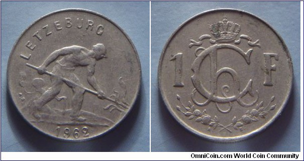 Luxembourg | 
1 Franc, 1962 | 
21 mm, 4 gr. | 
Copper-nickel | 

Obverse: Man shoveling coal, date belown | 
Lettering: LETZEBURG 1962 |

Reverse: Crowned Monogram of Charlotte divides denomination | 
Lettering: Ch 1F. |