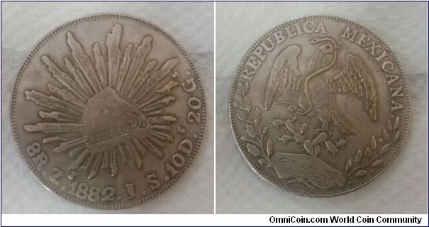 1882 Mexican Eagle Silver Peso Coin, Obverse: REPUBLICA MEXICANA (Republic of Mexico), the Mexican coat of arms featuring a golden eagle eating a snake on top of a prickly pear cactus surrounded with oak tree branches and leaves beneath; Reverse: LIBERTAD (freedom) inscribed on Liberty Cap, 8R. Z. 1882. J. S. 10D. 20G.1882