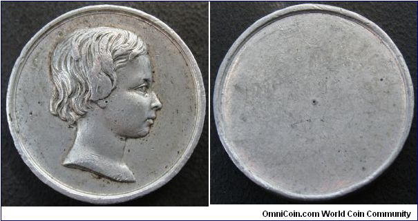 This is a trial strike in WM 32mm. of the obverse of THE PRINCE OF WALES (ALBERT EDWARD) BHM# 2384 before 1850 was added below the bust. In 1850 L. C. Wyon engraved a set of 7 medals of the Royal Children BHM#'s 2384 to 2390, in silver very rare, in bronze rare.BHM states that Unifaced trial strikings of the obverses of these pieces exist in white metal 
They make no reference as to rarity of these trial strikes but I suspect they must be extremely rare.